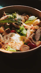 A colorful bowl of fresh salad with mixed greens, grilled chicken, cherry tomatoes, and a drizzle of creamy dressing.