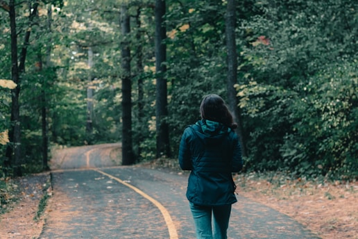 woman in green jacket walking on pathway between trees during daytime