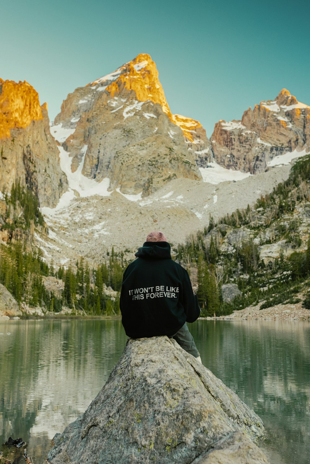 昼間、湖の近くの岩の上に座っている黒いジャケットを着た人