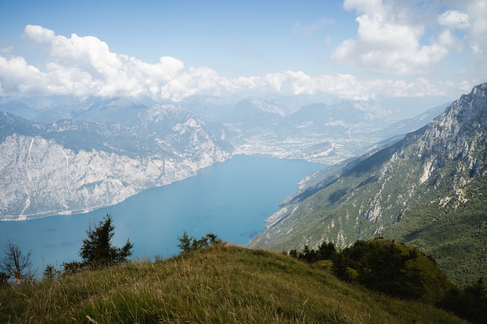 campo de hierba verde cerca del lago y la montaña bajo nubes blancas y cielo azul durante el día