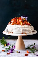A close-up of a pavlova topped with fresh fruits and a drizzle of sauce.