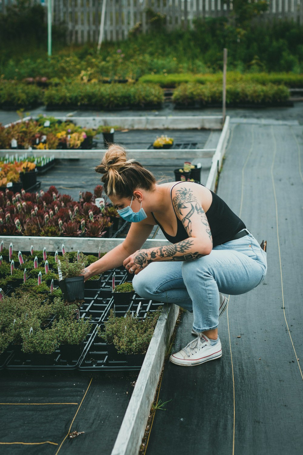 woman in white tank top and blue denim jeans sitting on black metal railings during daytime