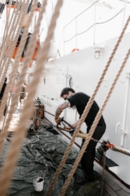 A skilled worker restoring the wooden deck of a small houseboat under bright daylight.