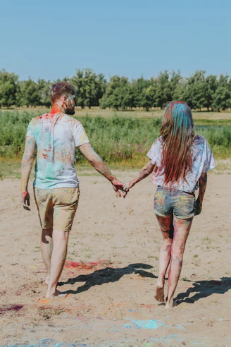 man and woman holding hands while walking on brown sand during daytime