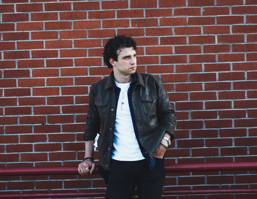 man in black leather jacket standing beside red brick wall