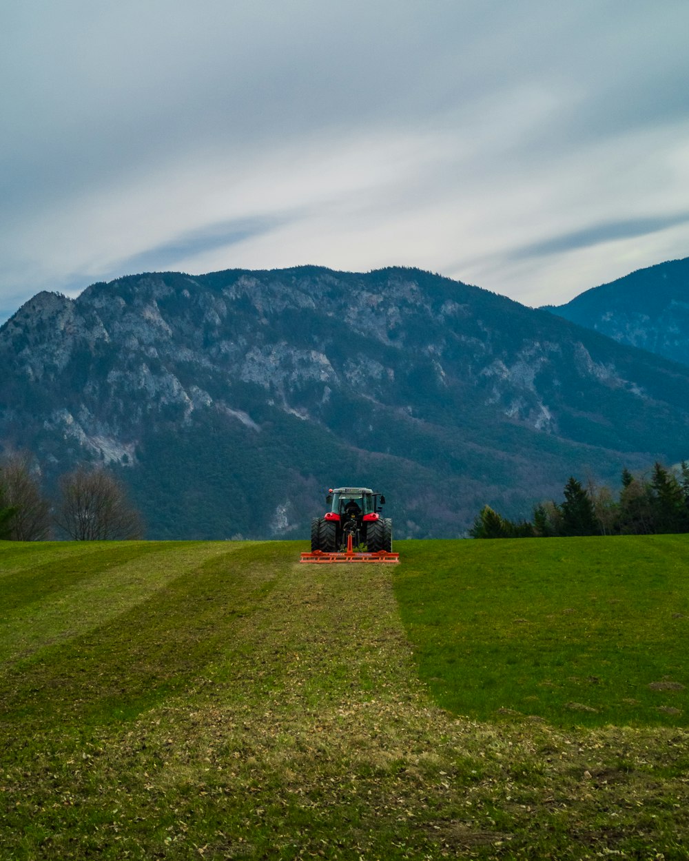 tractor rojo y negro en el campo de hierba verde cerca de la montaña durante el día