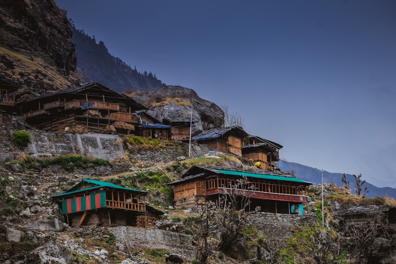 brown and green house near mountain under blue sky during daytime