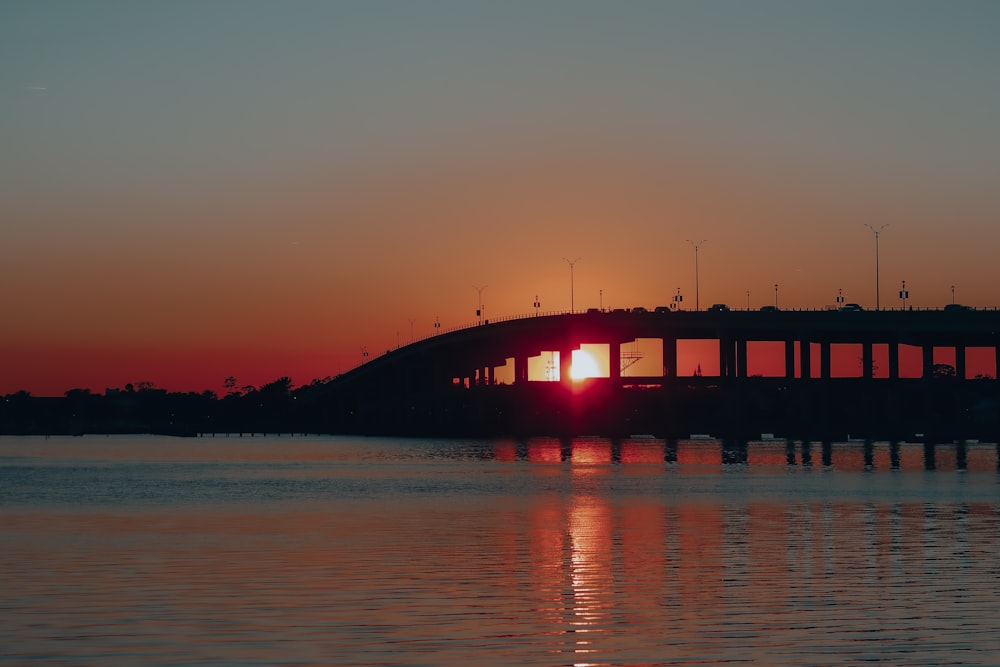 silhouette of bridge over body of water during sunset