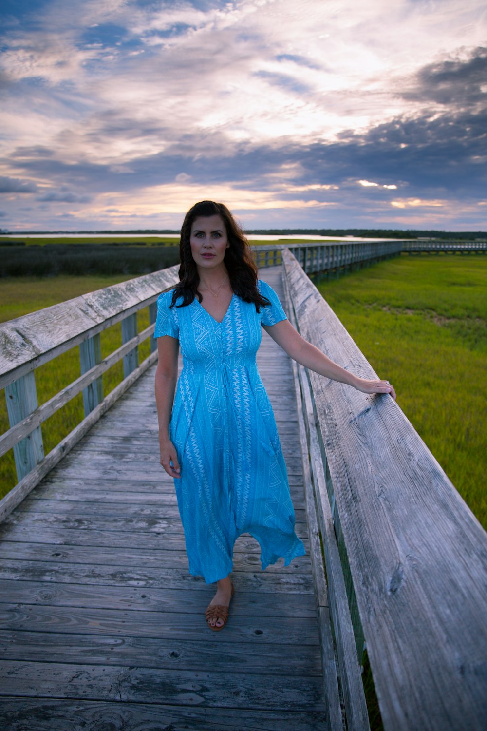 woman in blue dress standing on wooden bridge