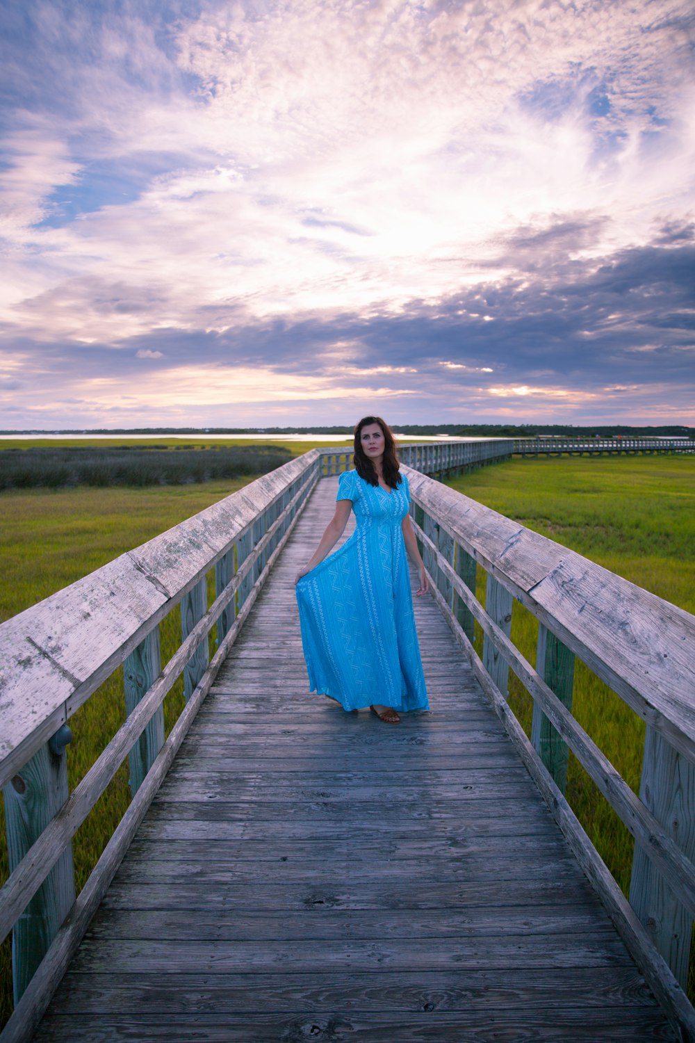 Mujer con vestido azul de pie en un puente de madera