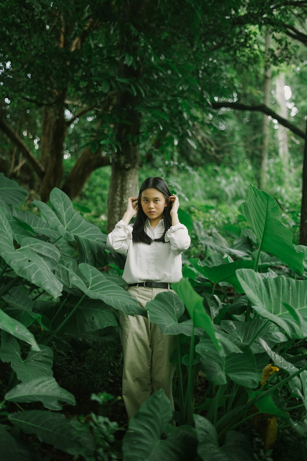 흰색 긴 소매 셔츠와 녹색 바지에 녹색 식물에 앉아 있는 여자