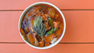A bowl of rich and tender rendang served with steamed white rice on a rustic wooden table.