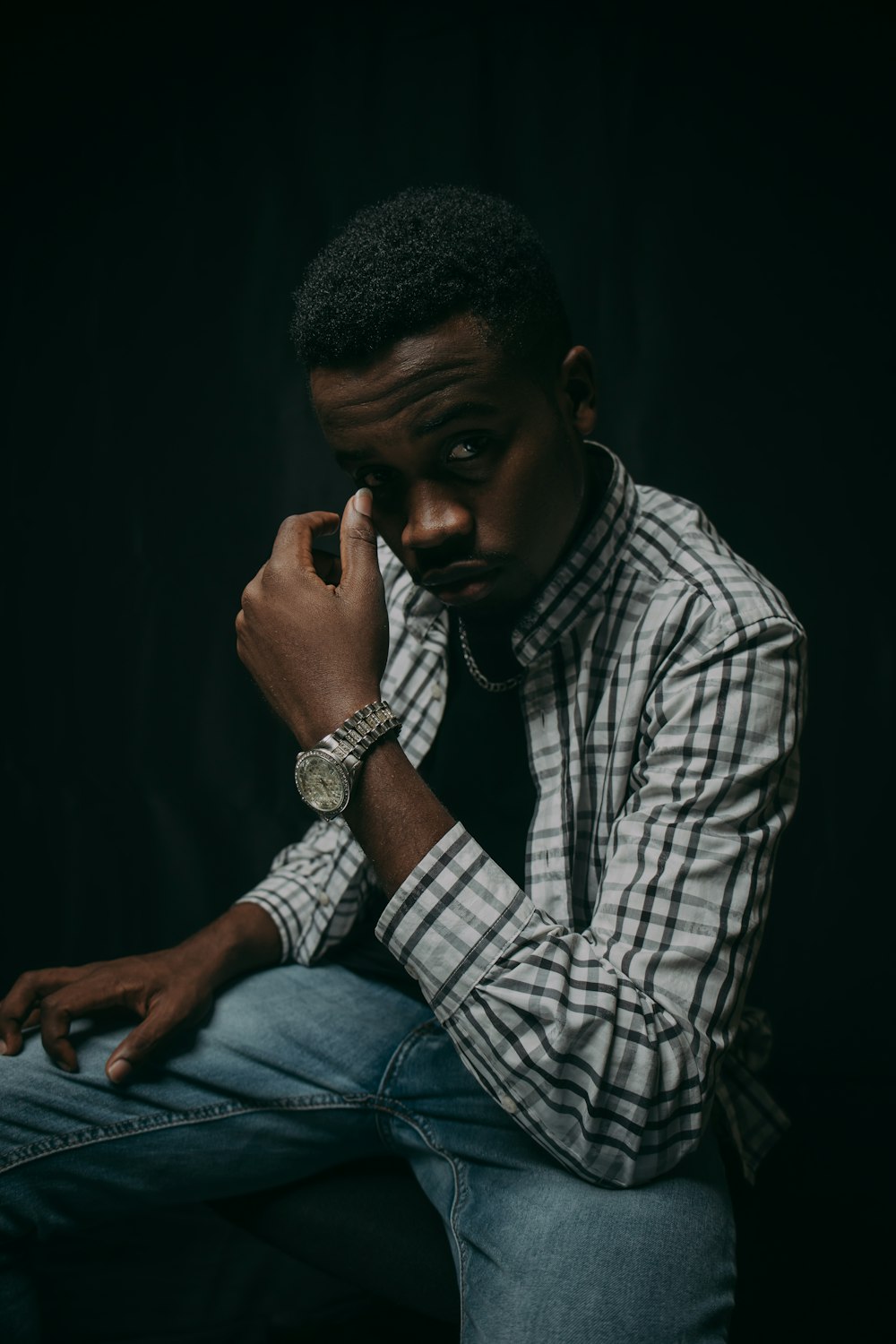 man in white and black plaid dress shirt and blue denim jeans sitting