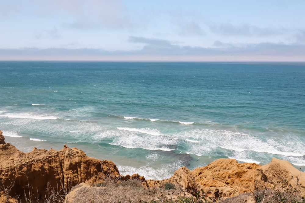 brown rocky mountain beside blue sea under white clouds during daytime