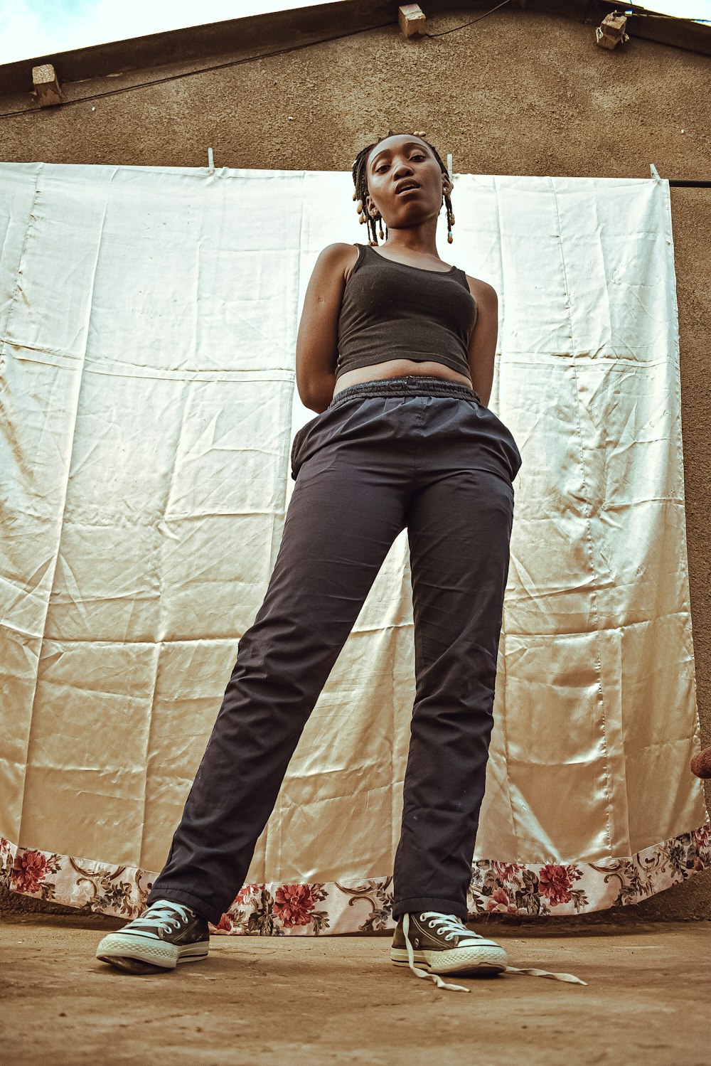 Femme en débardeur gris et jean bleu debout à côté d’un mur blanc