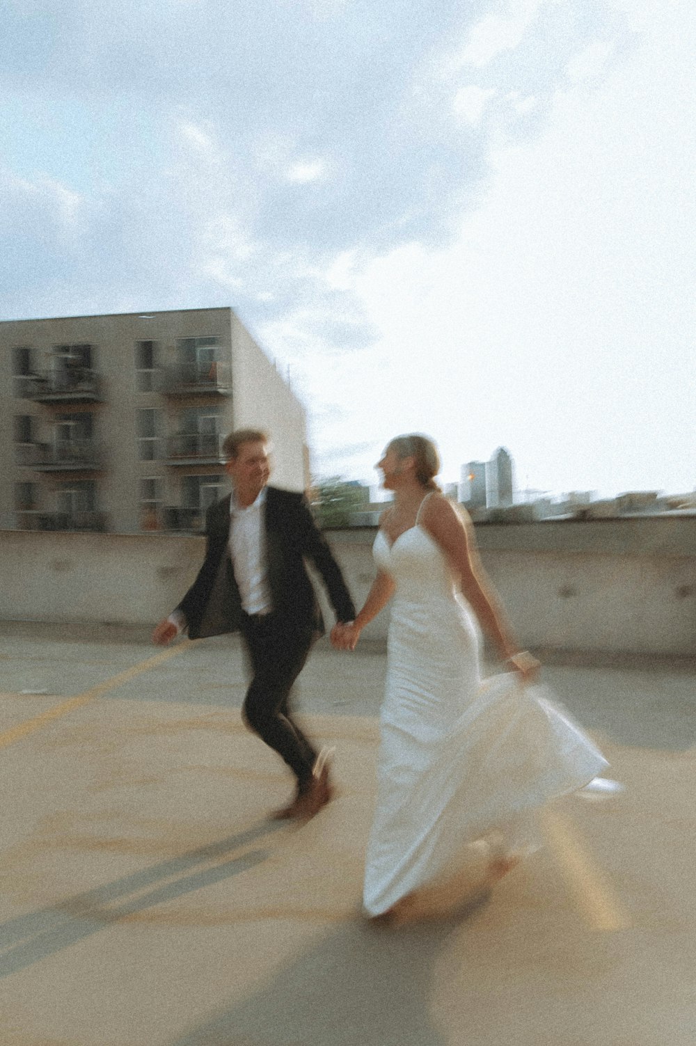 man in black suit jacket and woman in white dress walking on brown concrete floor during
