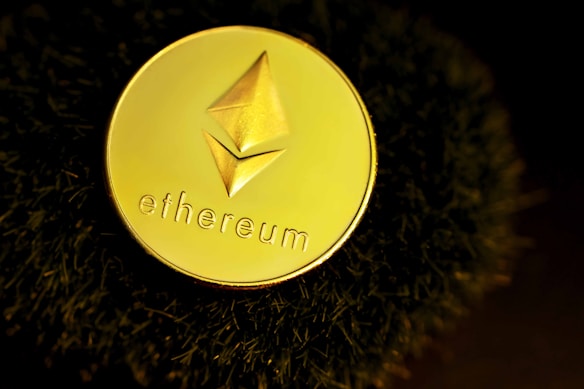 A golden coin featuring the Ethereum logo and text rests against a dark, textured surface. The lighting creates a dramatic, luxurious feel with reflective highlights on the coin.