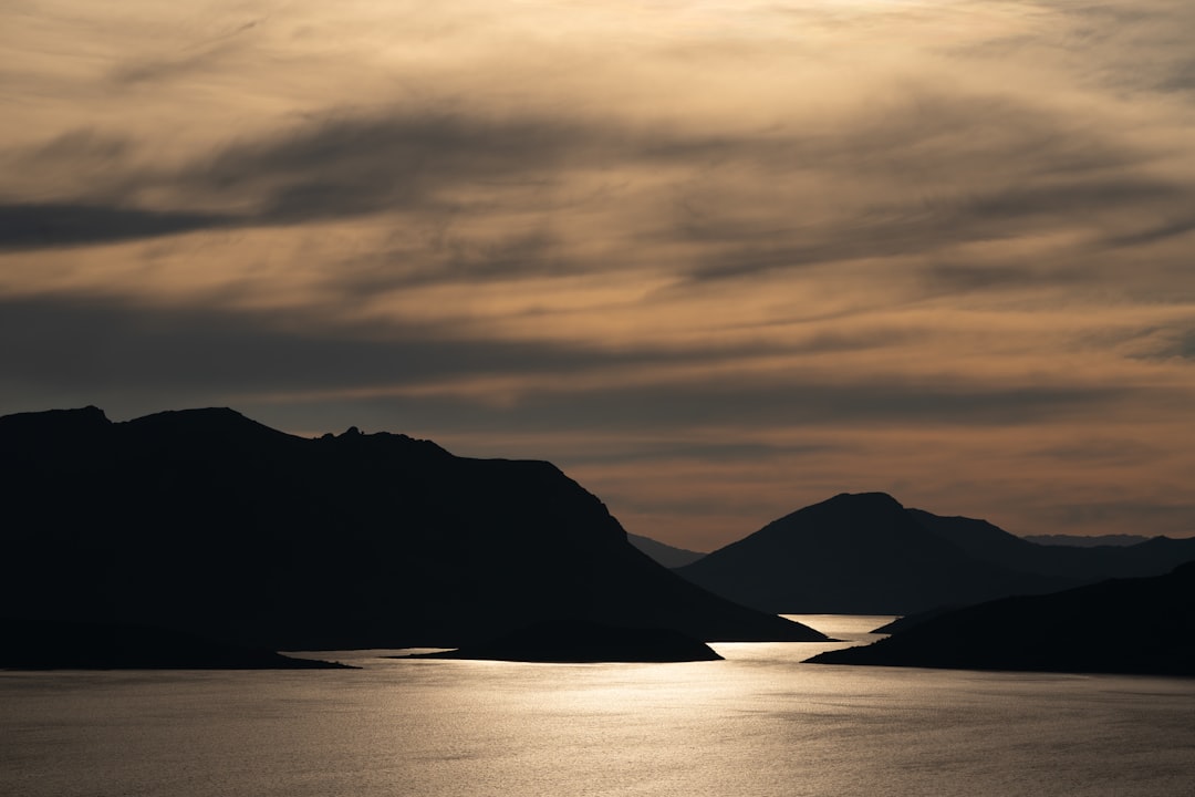 silhouette of mountain near body of water during sunset