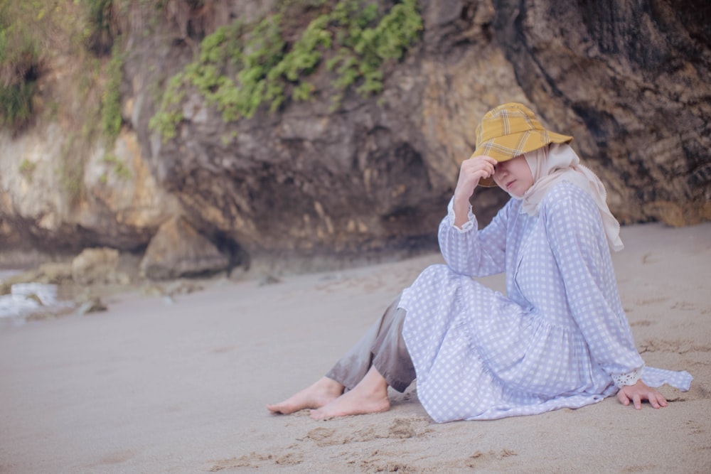 woman in white and blue dress sitting on brown sand during daytime