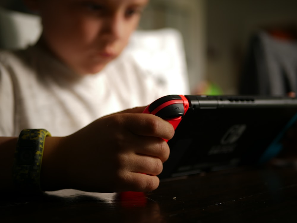 boy in white crew neck t-shirt holding black and red cordless device