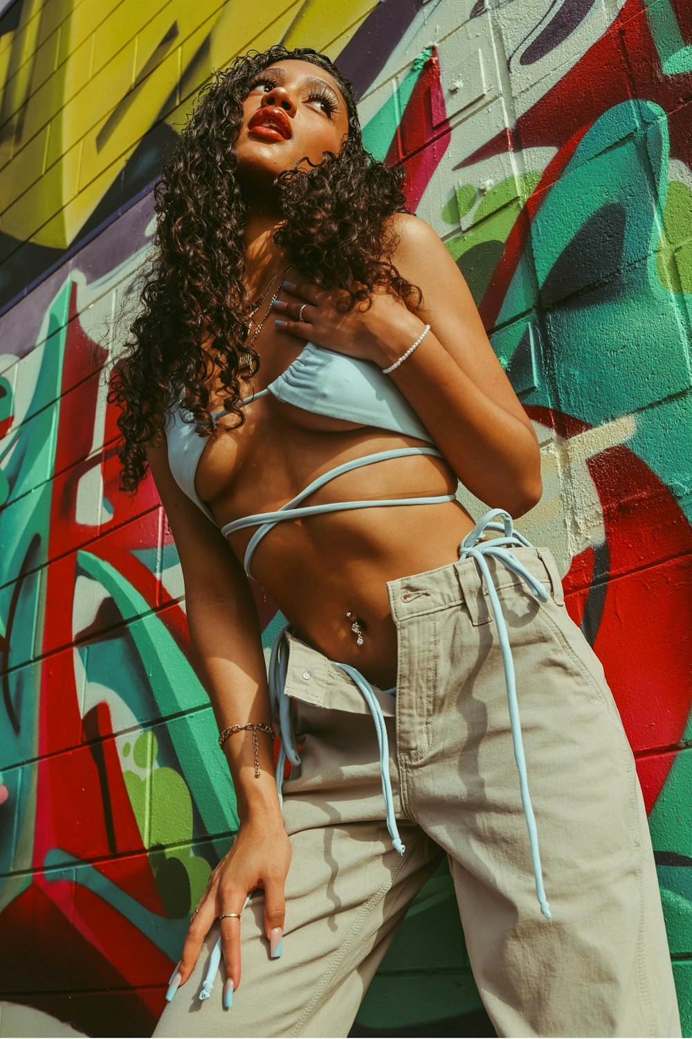 woman in white spaghetti strap top and gray denim shorts standing beside green and red wall