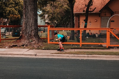 man in blue t-shirt and black pants riding on black kick scooter on road during