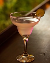 An elegant cocktail glass filled with a tequila-based drink, set against a softly lit background.