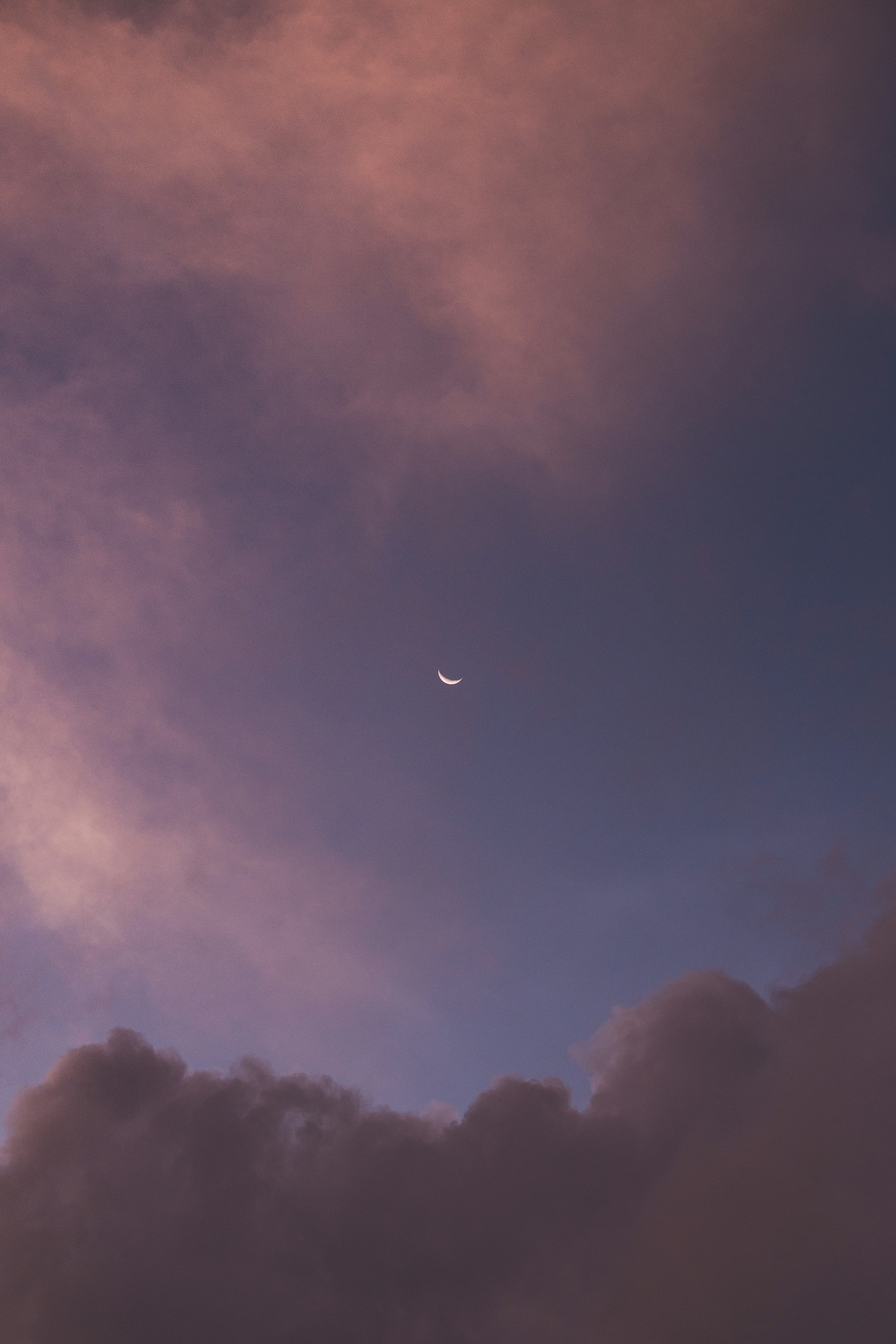 Moon with clouds basked in the light of the setting sun.