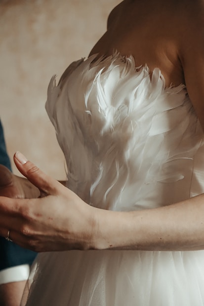 An elegant dress with a feathered texture around the bodice is highlighted. A person's hands are visible, partly outstretched.