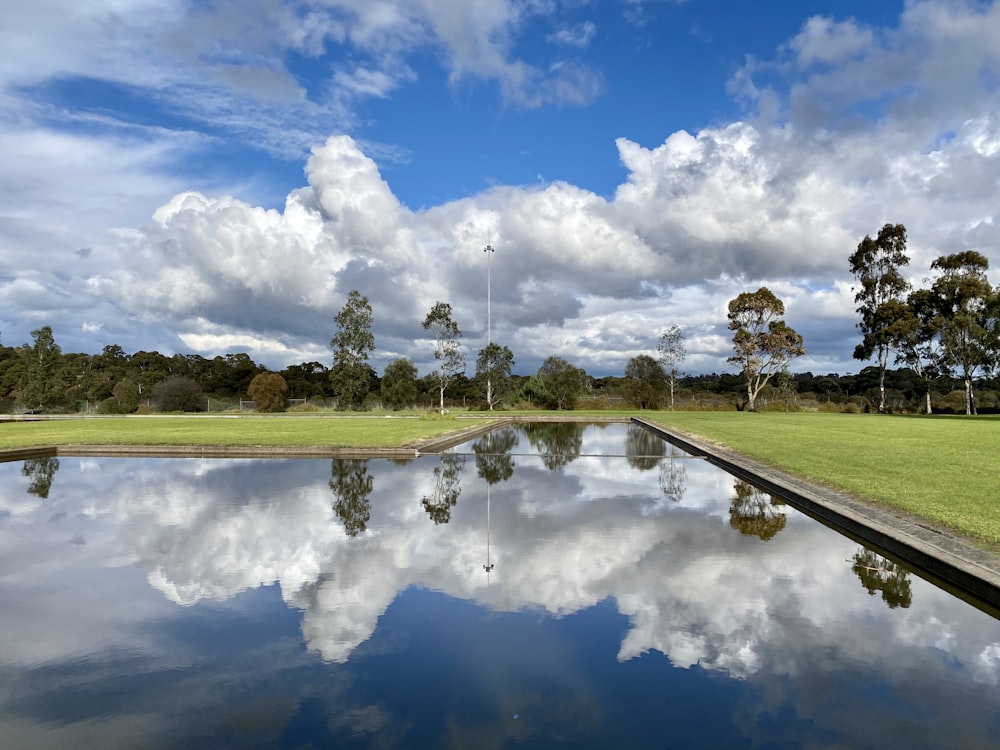 green grass field near lake under blue and white cloudy sky during daytime