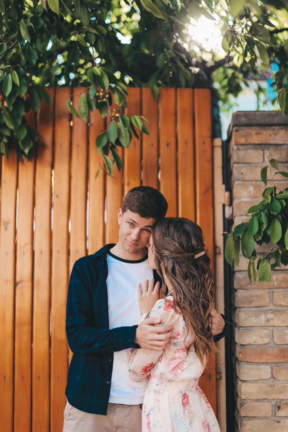 a man and woman standing next to each other in front of a wooden fence