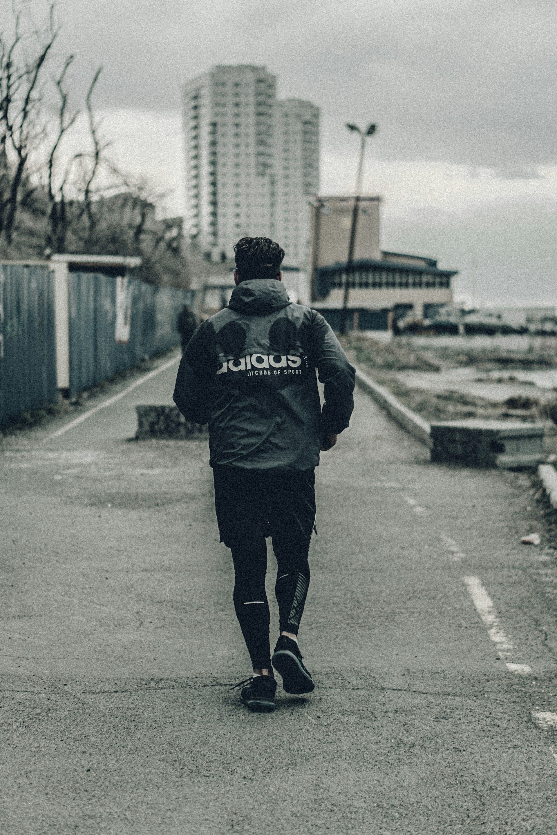 A runner in urban streetwear jogging on an asphalt city street at dawn, with buildings softly lit in the background, no visible shoe brands.