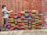 A brick wall features a colorful mural of various brightly painted bricks. To the left, a grayscale depiction of a child appears to be painting the bricks. The wall behind is made of traditional red bricks, with the painted section interrupting the uniformity with vibrant colors.