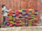 A brick wall features a colorful mural of various brightly painted bricks. To the left, a grayscale depiction of a child appears to be painting the bricks. The wall behind is made of traditional red bricks, with the painted section interrupting the uniformity with vibrant colors.