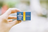 A hand holds a small blue and yellow box labeled with 'Mitsubishi Color Film ForPrints.' The background is blurred, focusing attention on the box.