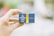 A hand holds a small blue and yellow box labeled with 'Mitsubishi Color Film ForPrints.' The background is blurred, focusing attention on the box.