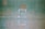 A green textured wall with the words 'NO NUKE' stenciled in orange paint. The words are centered in the upper portion of the image, and there are faint outlines of shapes or patterns below them.