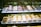 An assortment of beautifully decorated pastries and desserts displayed in a glass case. Each dessert is presented on individual trays with price tags, showcasing a variety of toppings such as berries, chocolate, and cream.