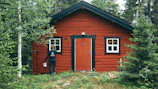 man in black jacket standing beside brown wooden house during daytime
