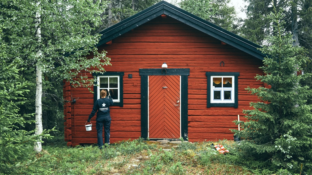 Hombre con chaqueta negra de pie junto a la casa de madera marrón durante el día