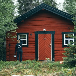 man in black jacket standing beside brown wooden house during daytime