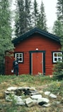 man in black jacket standing beside brown wooden house during daytime