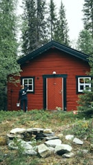 man in black jacket standing beside brown wooden house during daytime