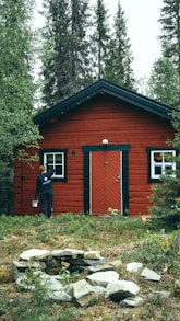 man in black jacket standing beside brown wooden house during daytime