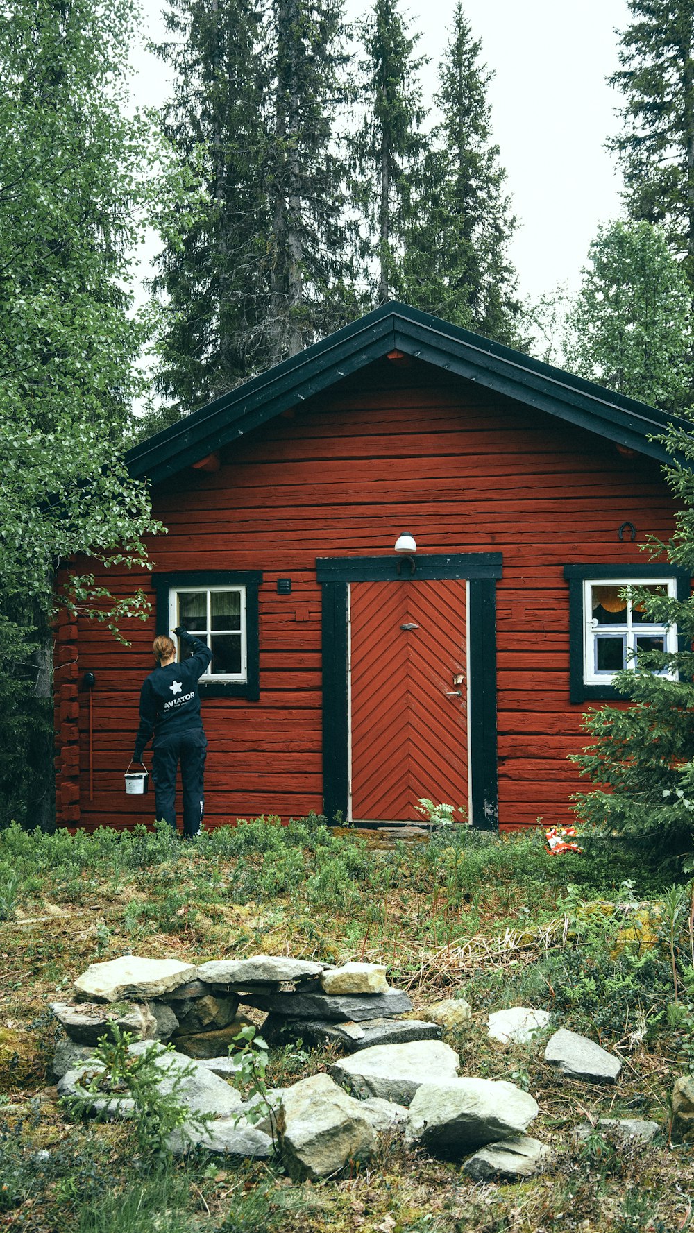 man in black jacket standing beside brown wooden house during daytime