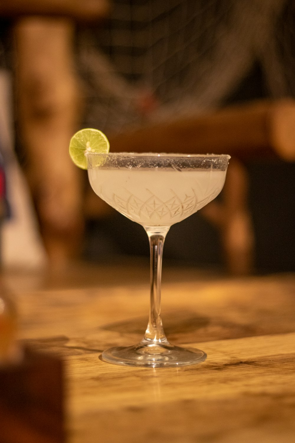 clear cocktail glass with green liquid and sliced lemon on brown wooden table