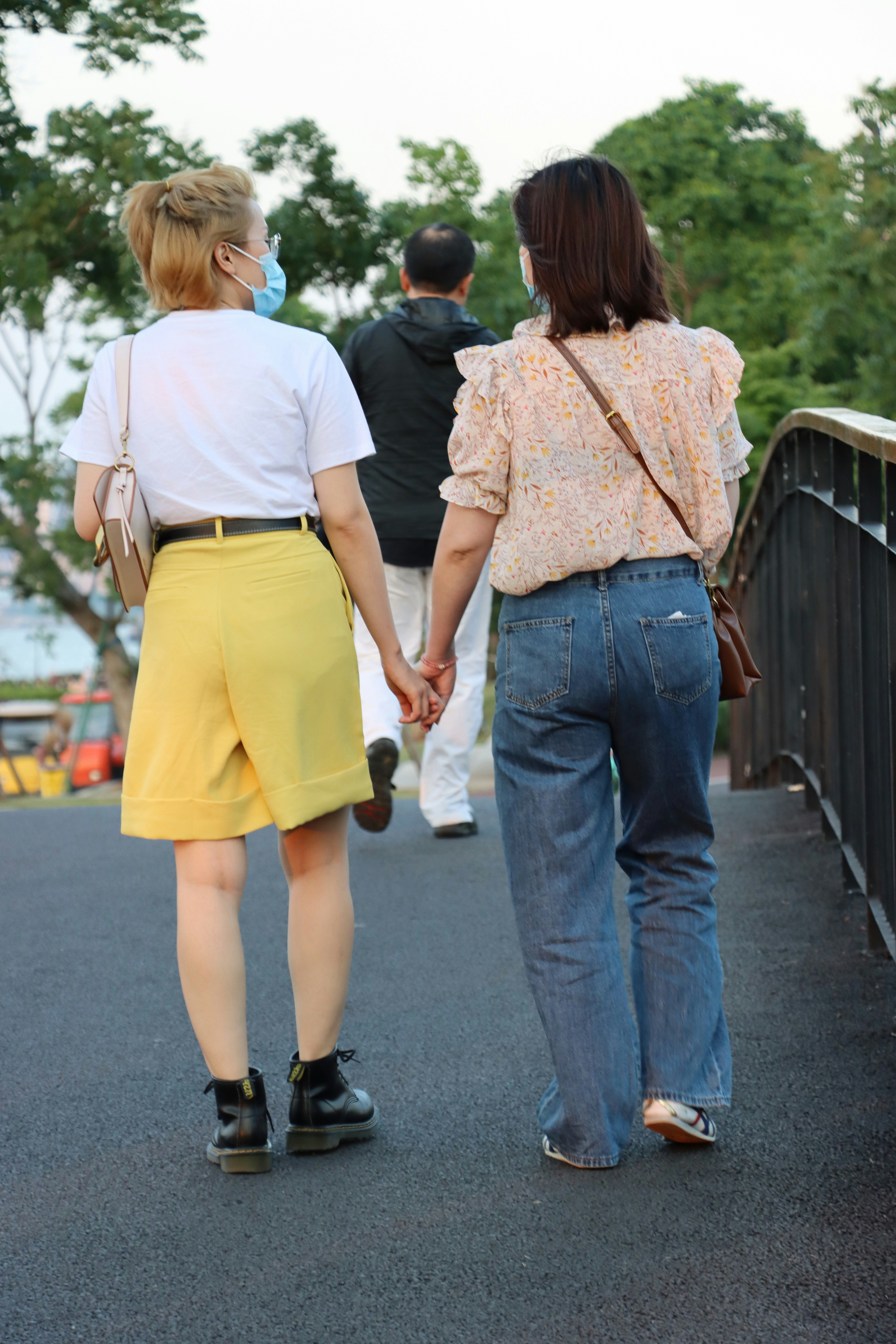 woman in yellow dress holding hands with woman in white t-shirt walking on sidewalk during