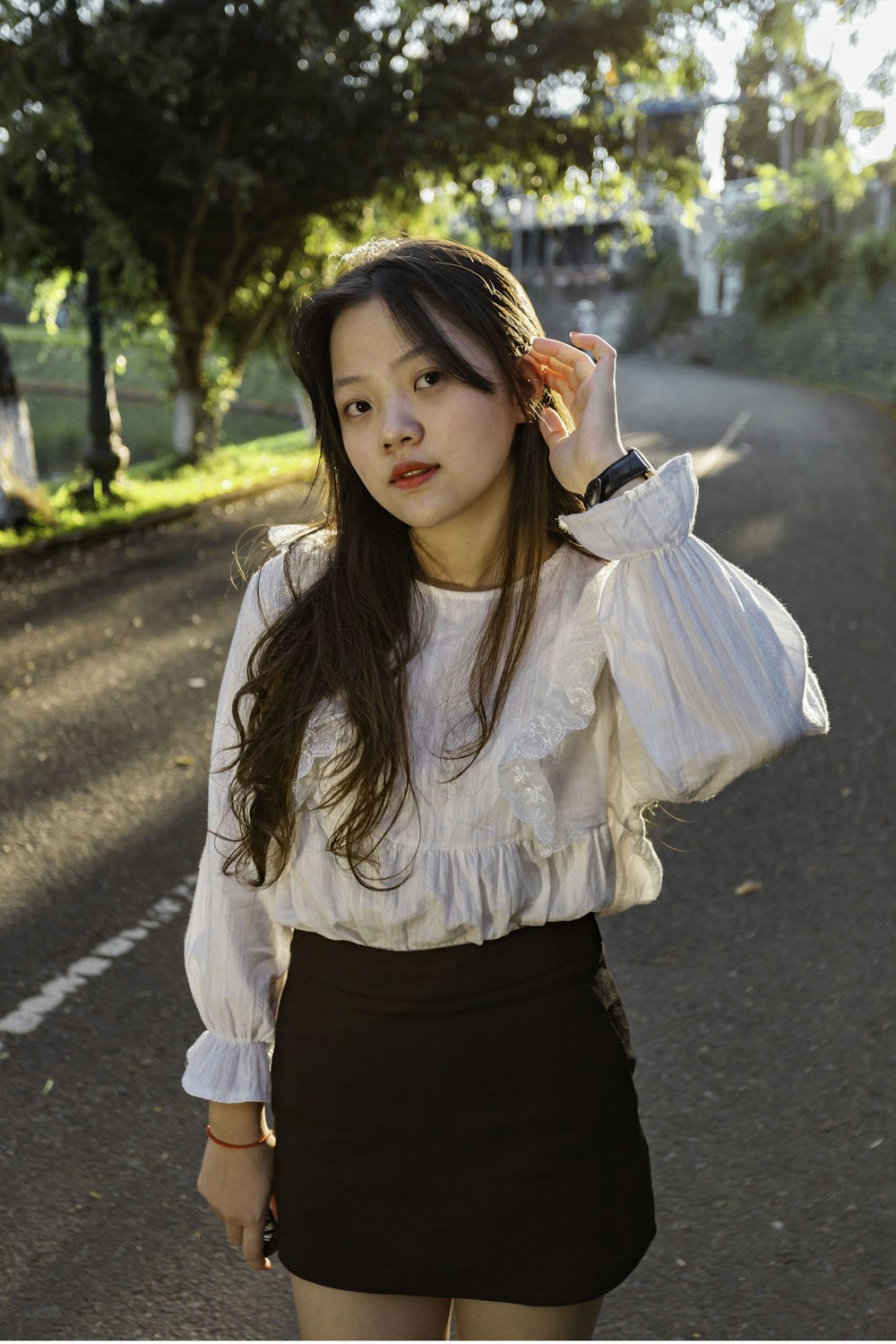 girl in white long sleeve shirt and black skirt standing on road during daytime