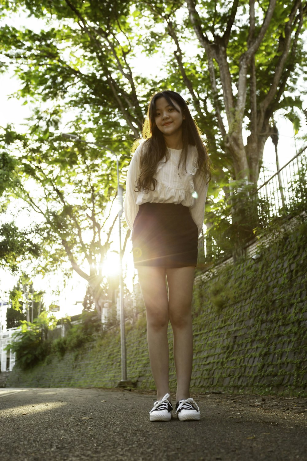 woman in white long sleeve shirt and black skirt standing near green trees during daytime