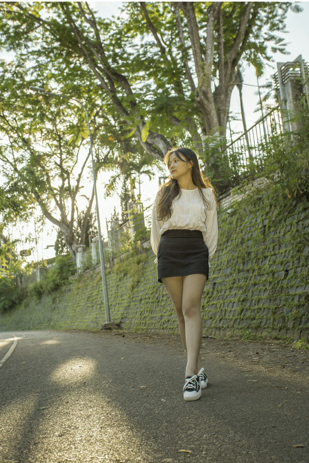 woman in white long sleeve shirt and black skirt standing on gray concrete road during daytime